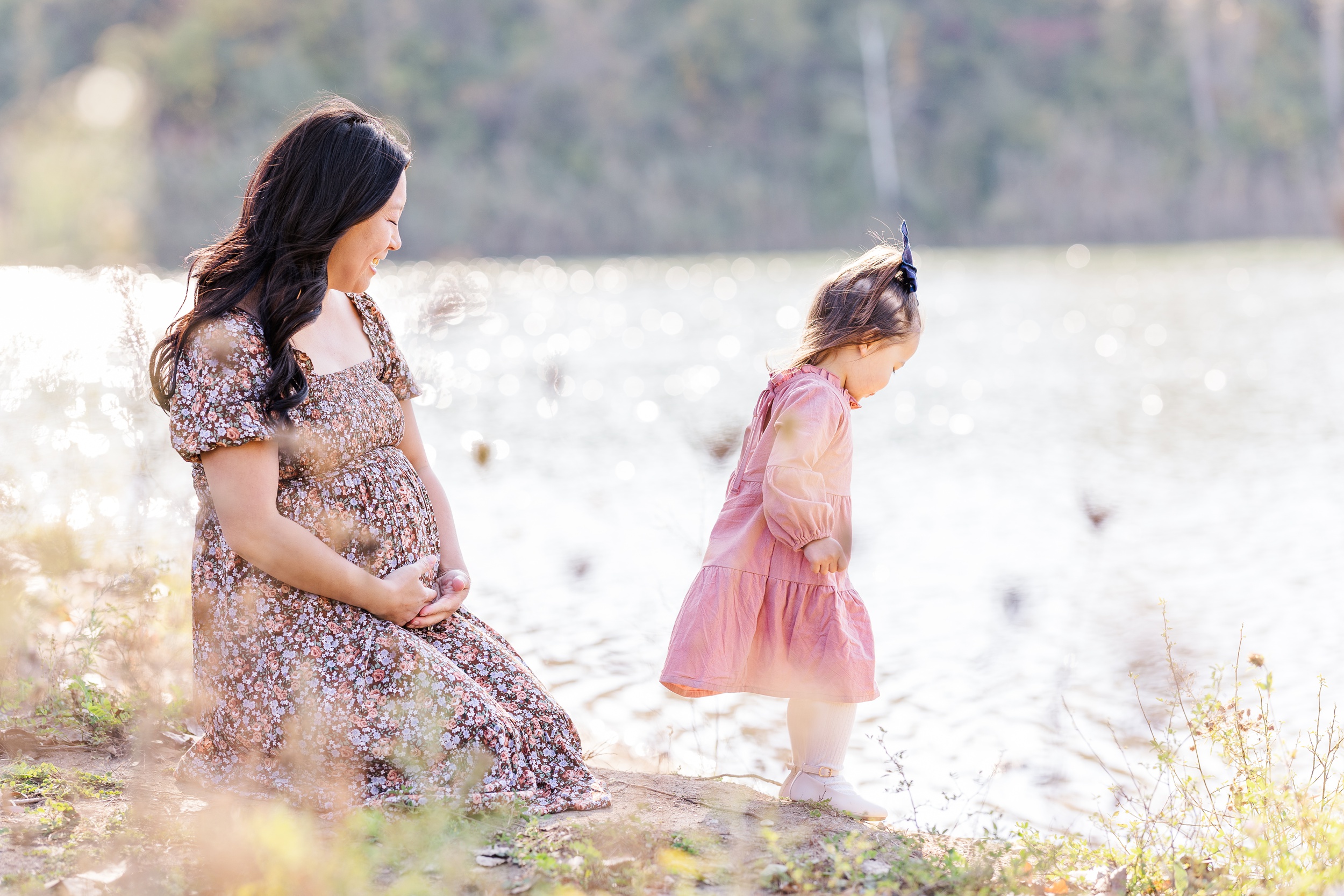 A happy pregnant mom explores the lakeshore with her toddler daughter in a pink dress after meeting ann arbor doulas