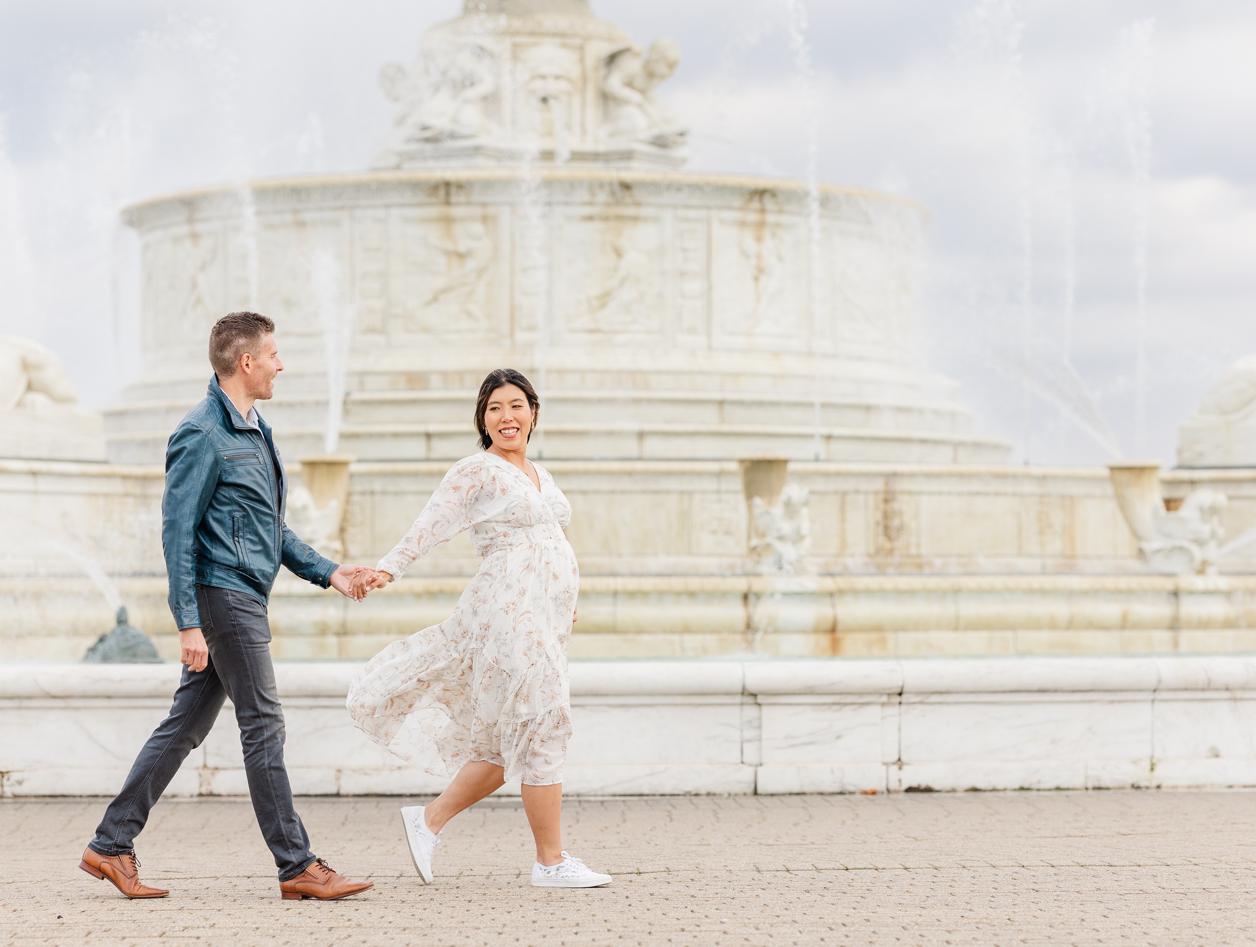 A pregnant woman walks her husband by the hand past grand fountains