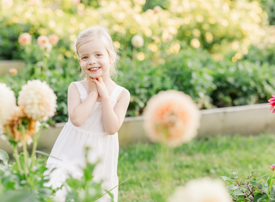 A smiling young girl in a white dress explores a flower garden at sunset