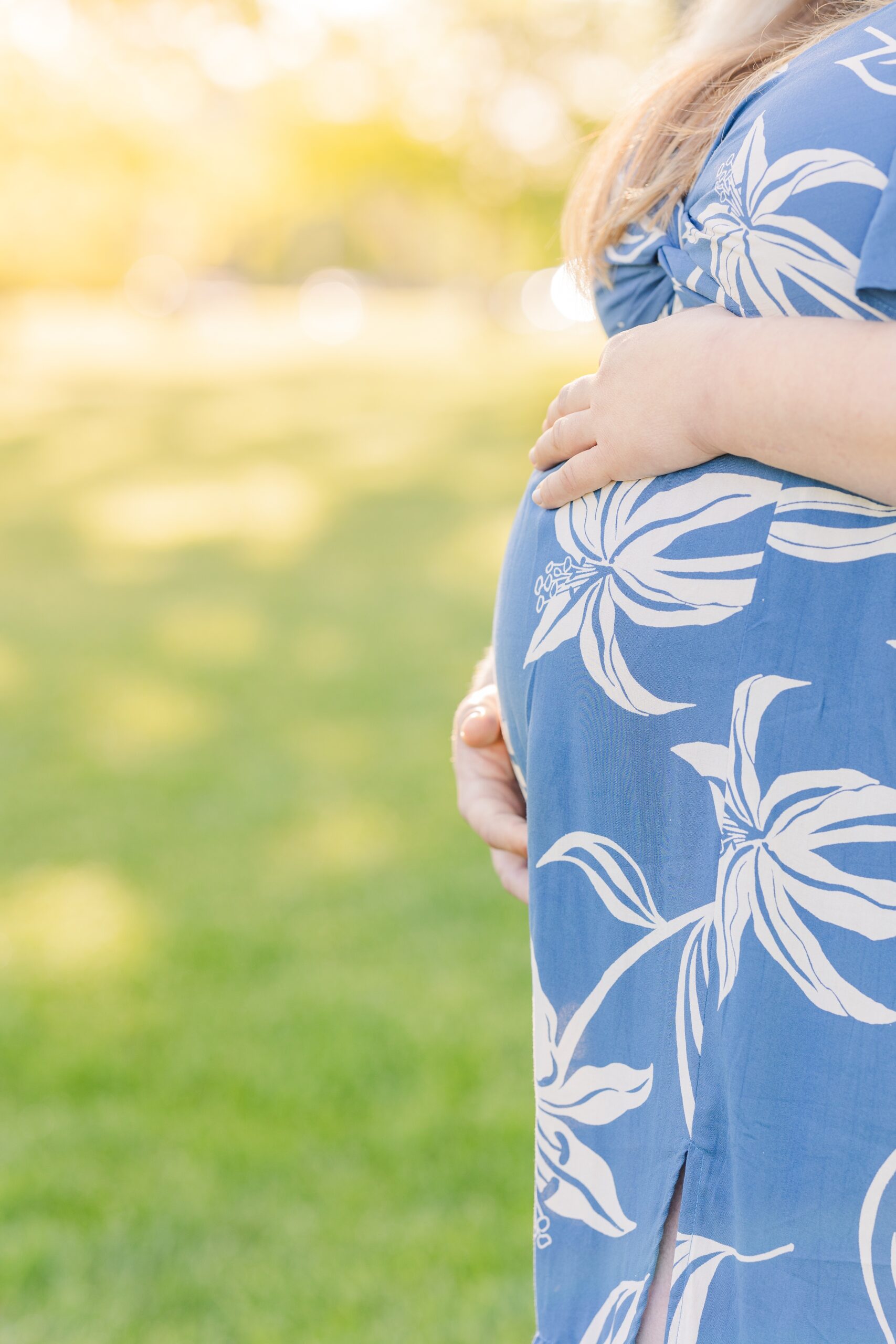 Details of a mom to be's bump with her hands on a it in a floral print maternity dress