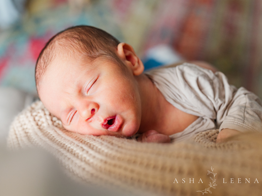 A newborn baby sleeps on a woven blanket in a onesie