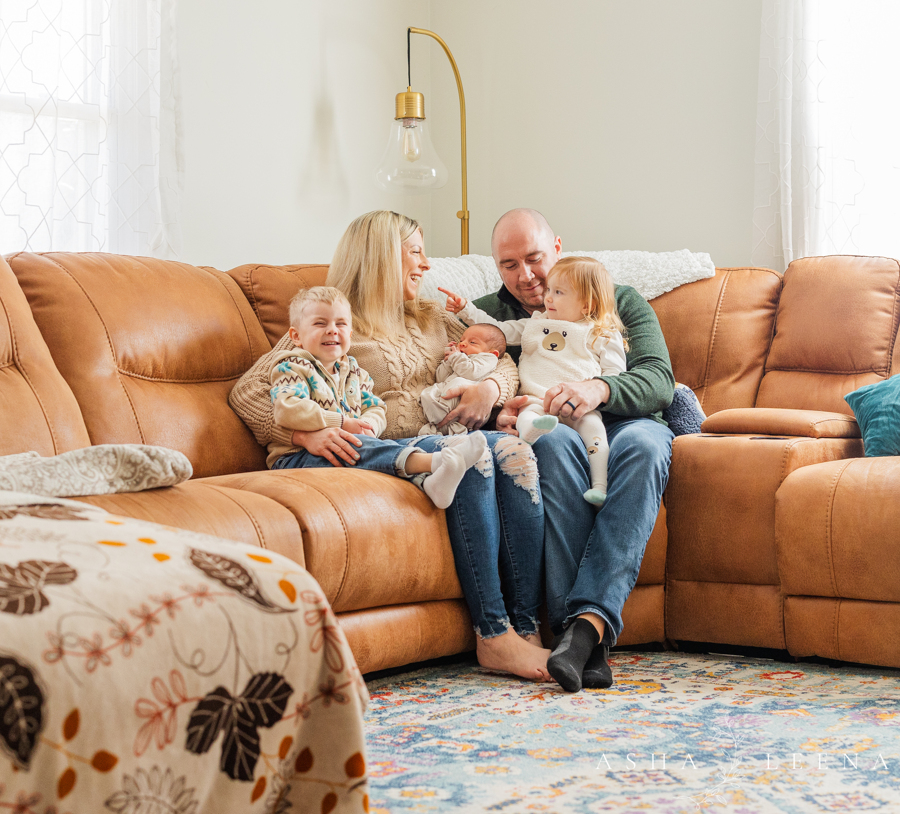 A happy family of 5 with 3 babies sit together on a leather couch after meeting a nanny in Ann Arbor