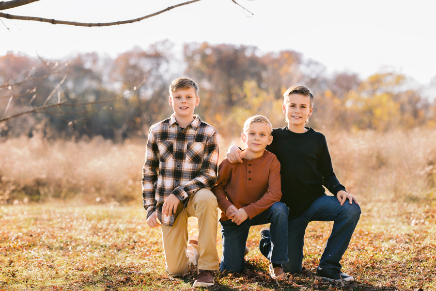 Three young brothers kneels in a field at sunset with arms around each other