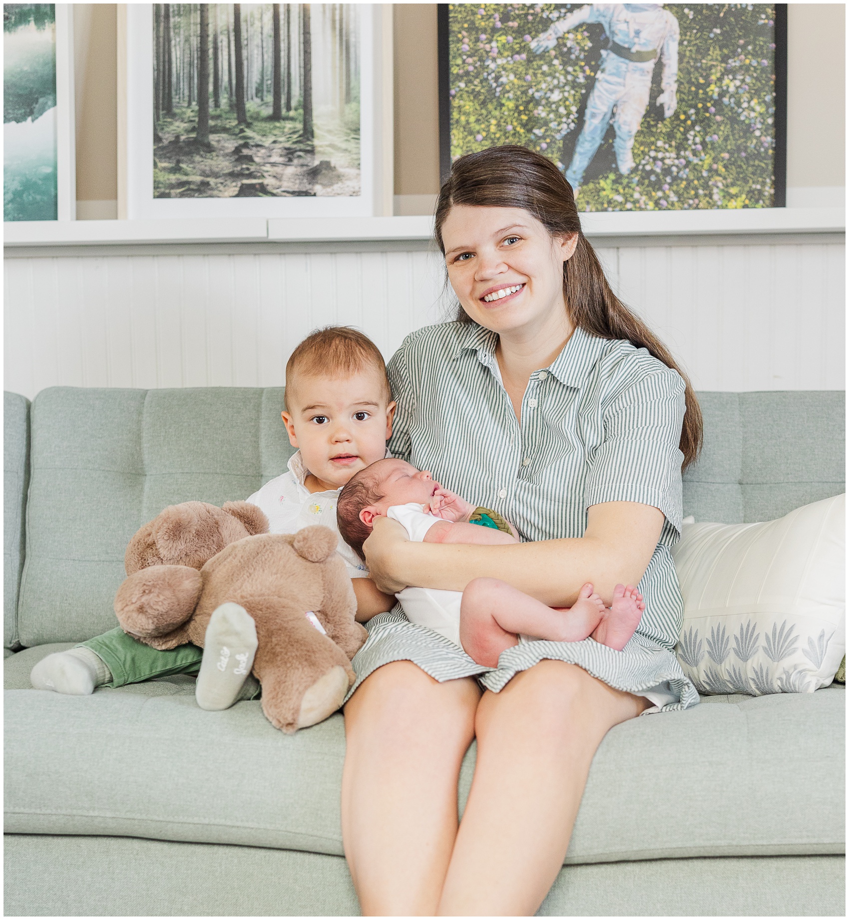 A smiling mother sits on a couch holding her newborn and toddler son thanks to ann arbor birth and family