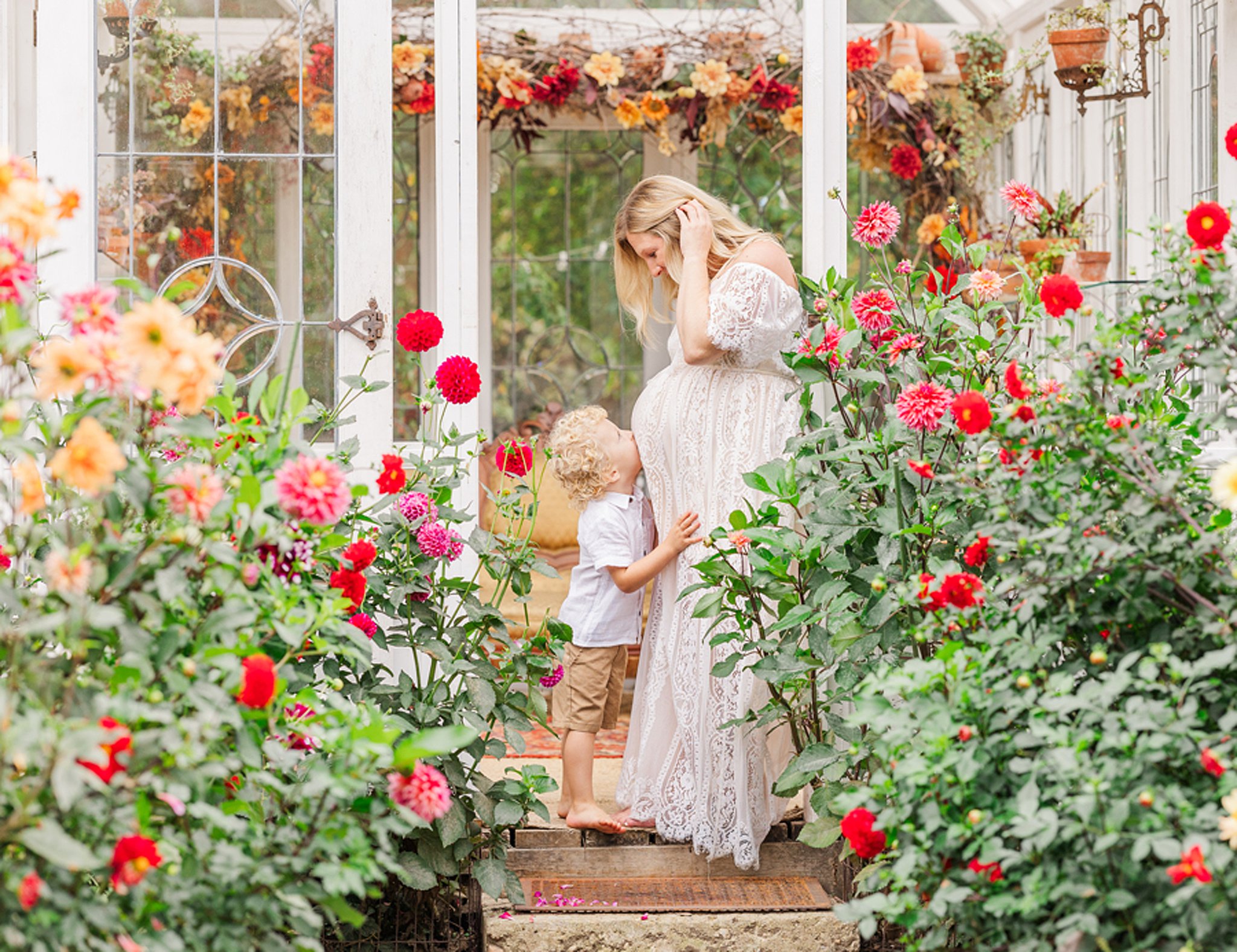 A toddler boy hugs and kisses mom's bump in a vibrant garden