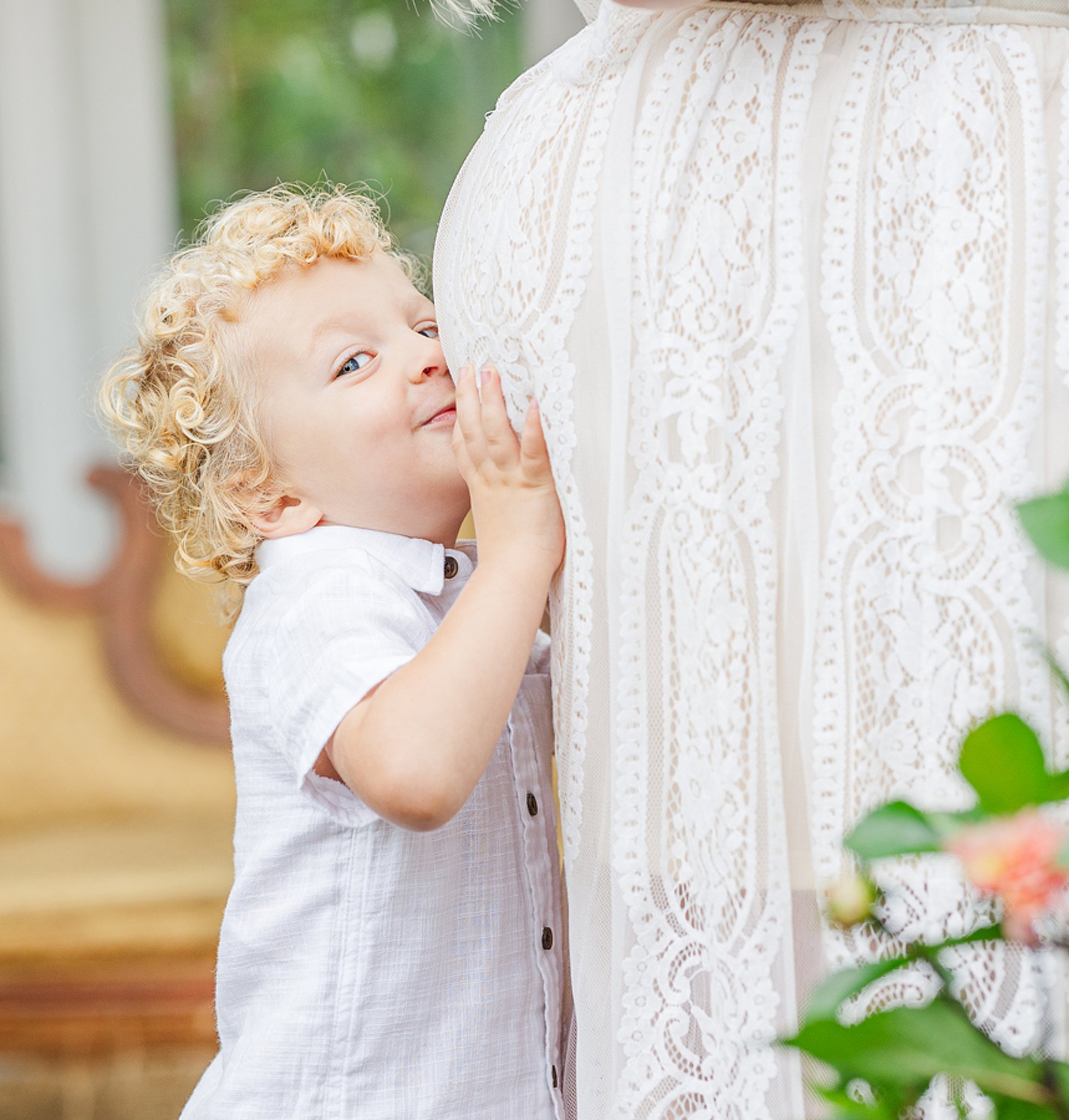 A toddler in a white shirt kisses mom's pregnant bump after a baby shower in ann arbor