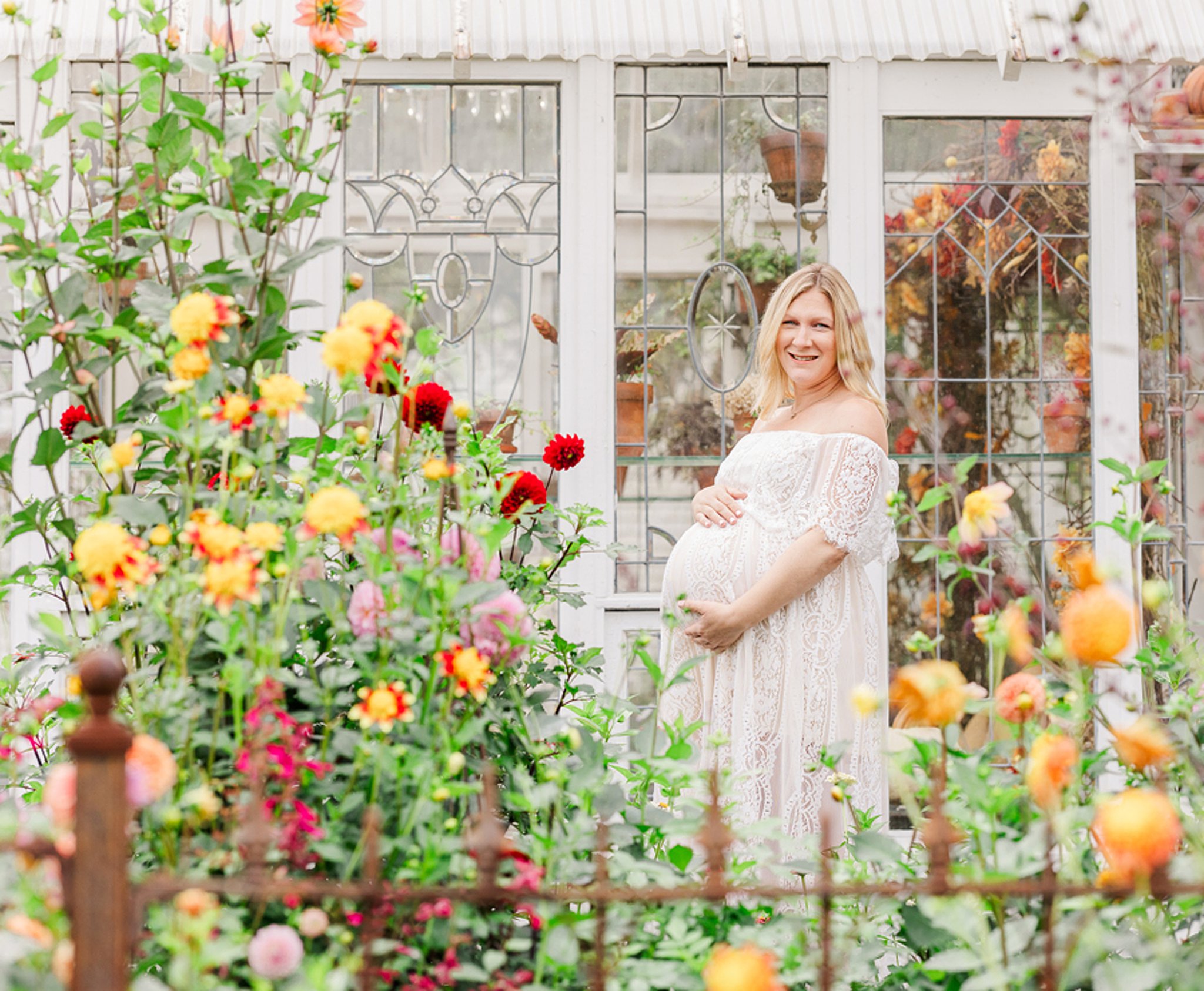 A happy mom to be in a lace maternity gown stands in a vibrant garden smiling after her baby shower in ann arbor