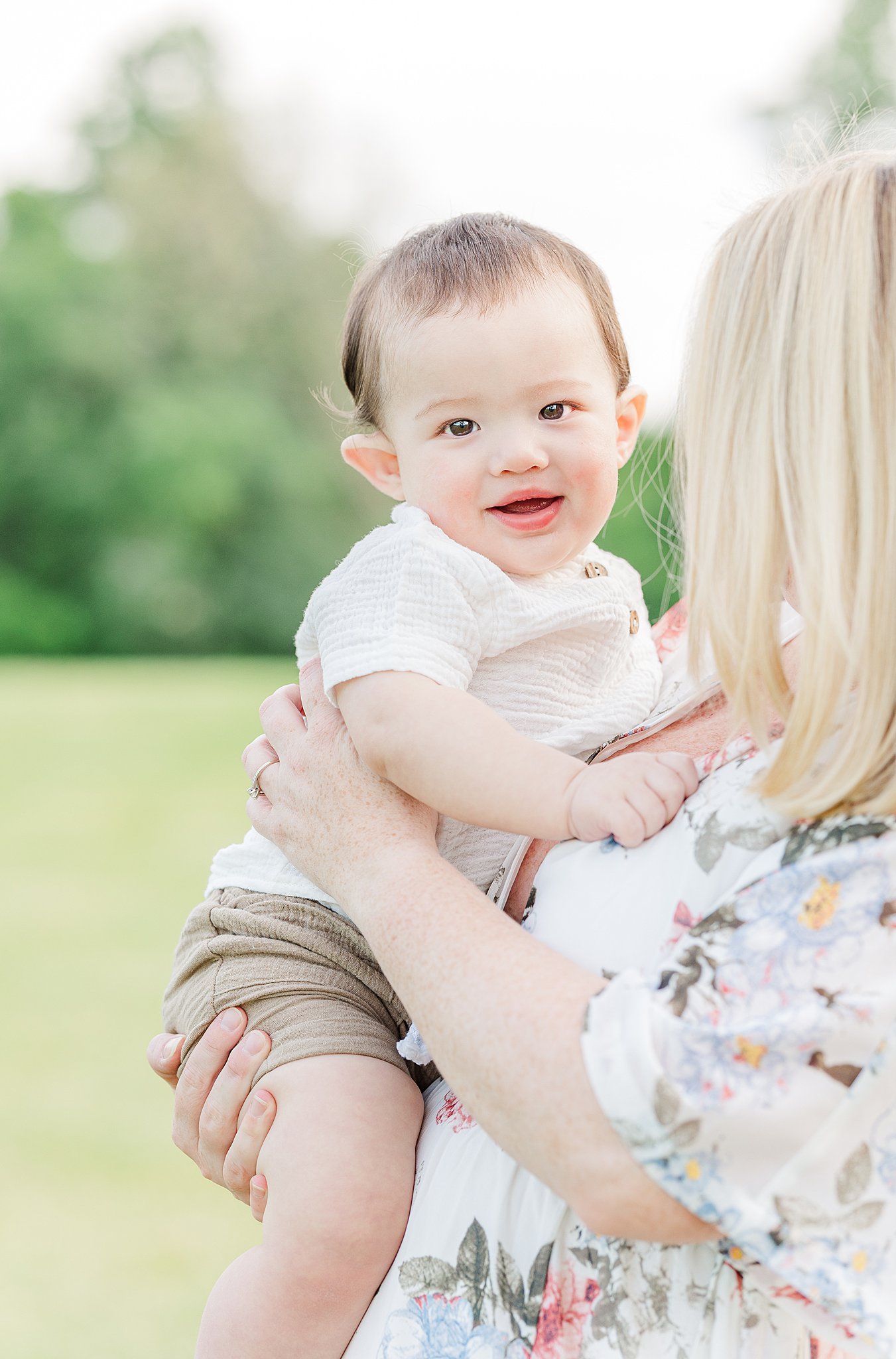 A baby sits in mom's arms smiling in a park