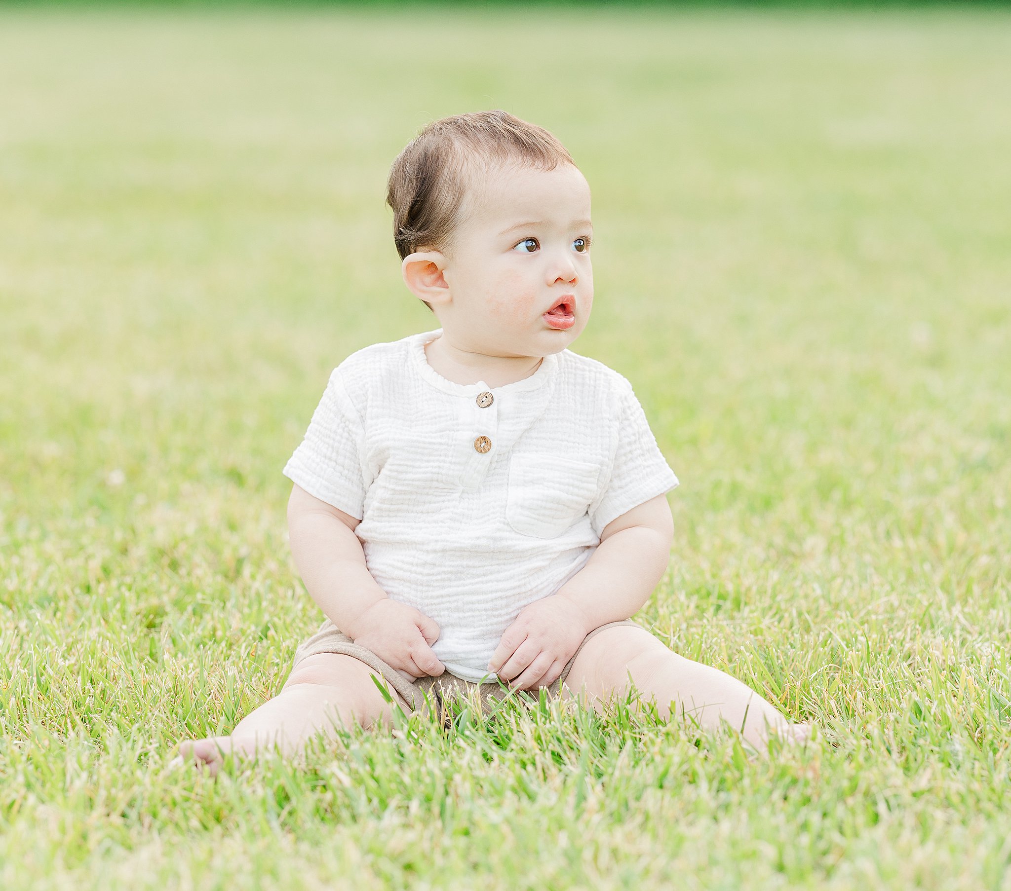 A baby sits in a lawn in a white shirt looking around after visiting baby stores in ann arbor