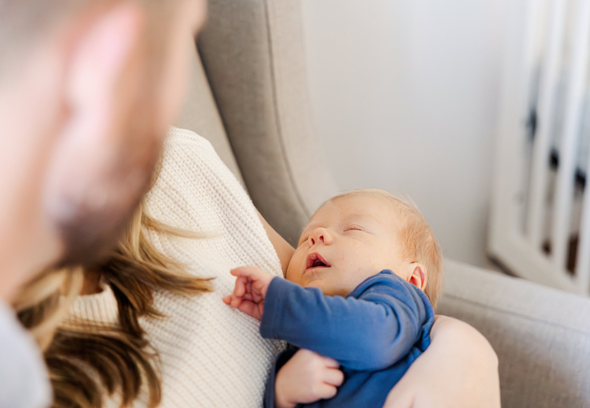 A newborn baby sleeps in mom's arms in a blue onesie in the nursery thanks to a lactation consultant in ann arbor