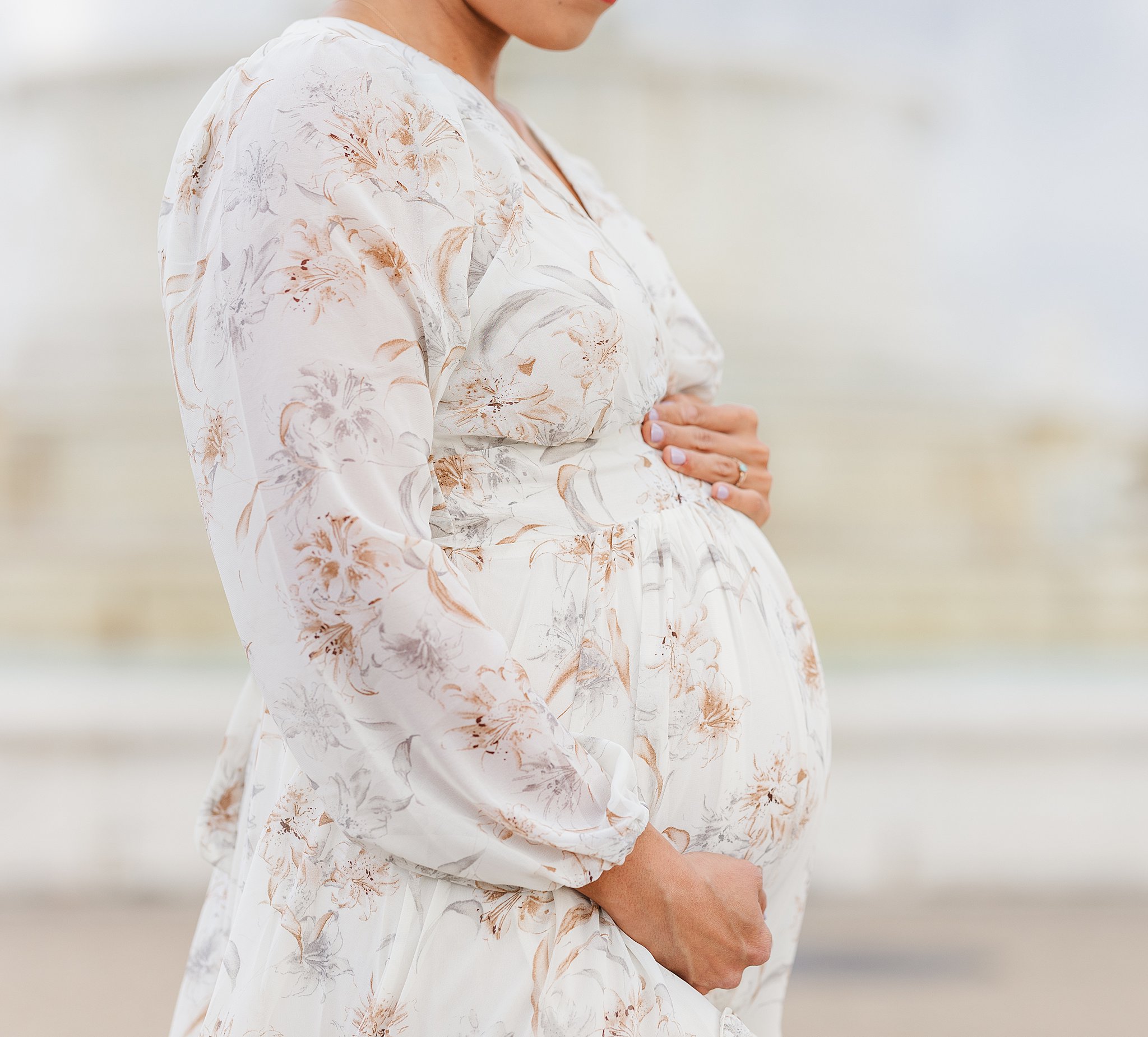 Details of a pregnant woman's bump in a floral print white maternity gown