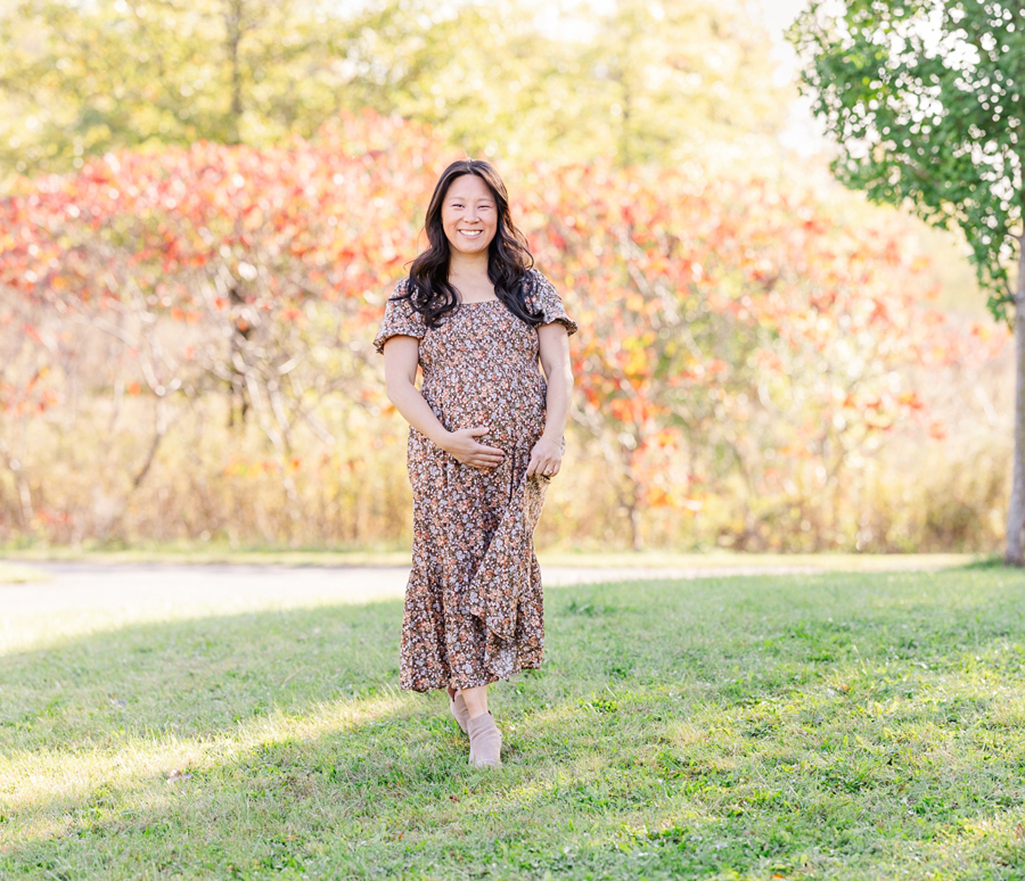 A mother to be in a floral print maternity dress walks in a park after visiting peek a bootique