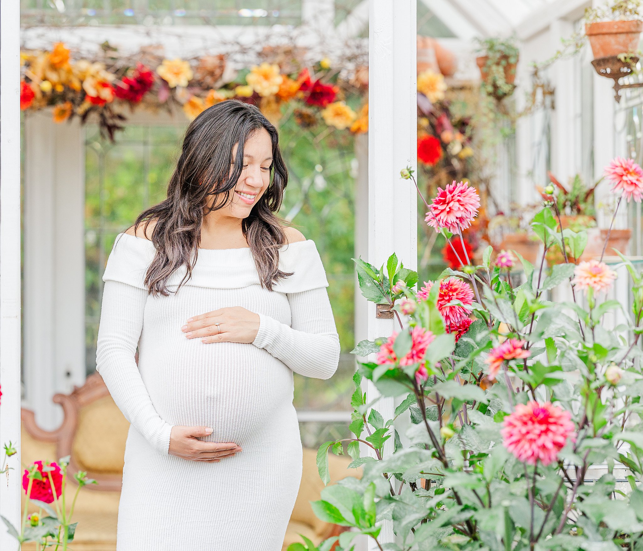 A mom to be explores a vibrant garden by a gazebo in a white gown