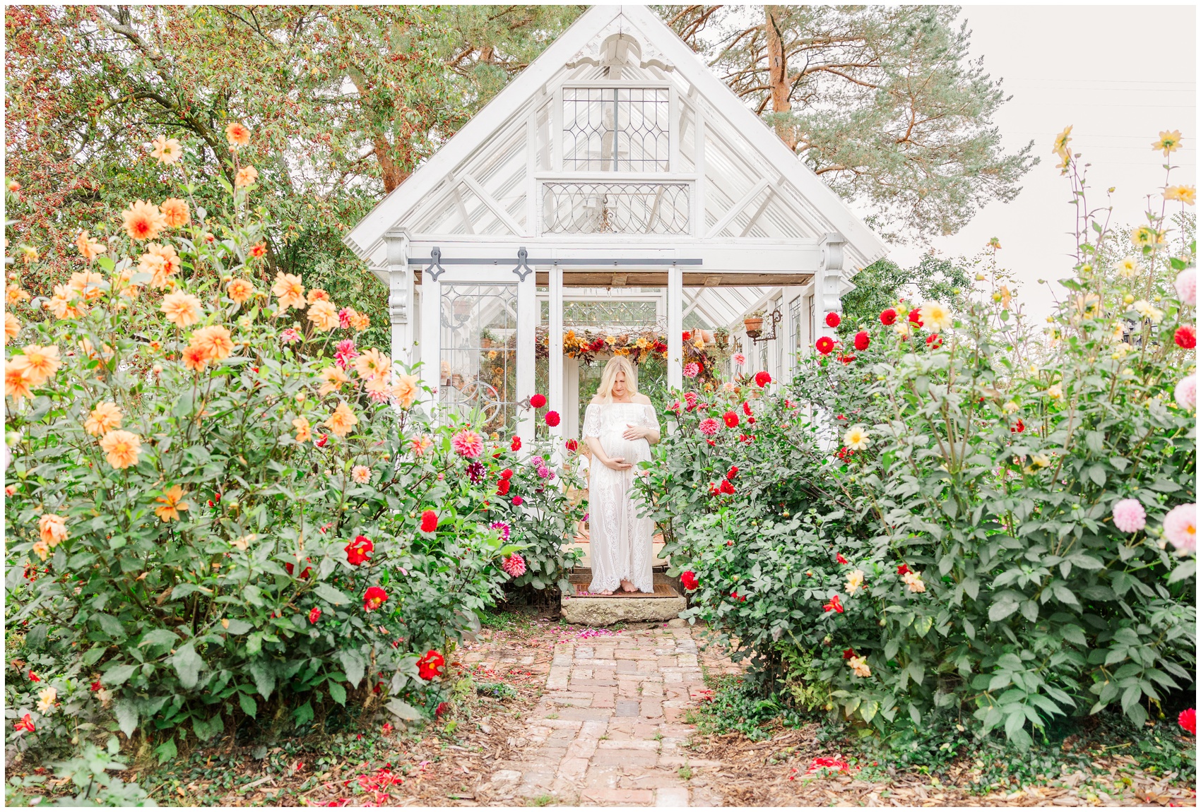 A pregnant woman walks in a flourishing garden out of a greenhouse in a white maternity dress after some prenatal pilates in ann arbor