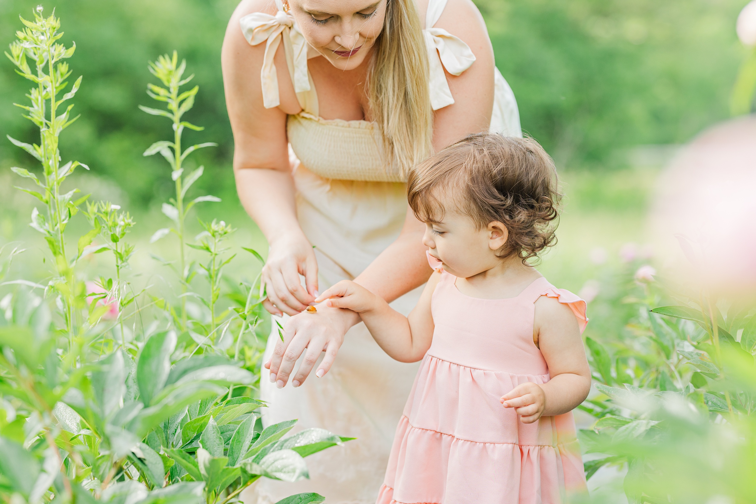 A young girl in a pink dress explores a ladybug on mom's hand in a garden