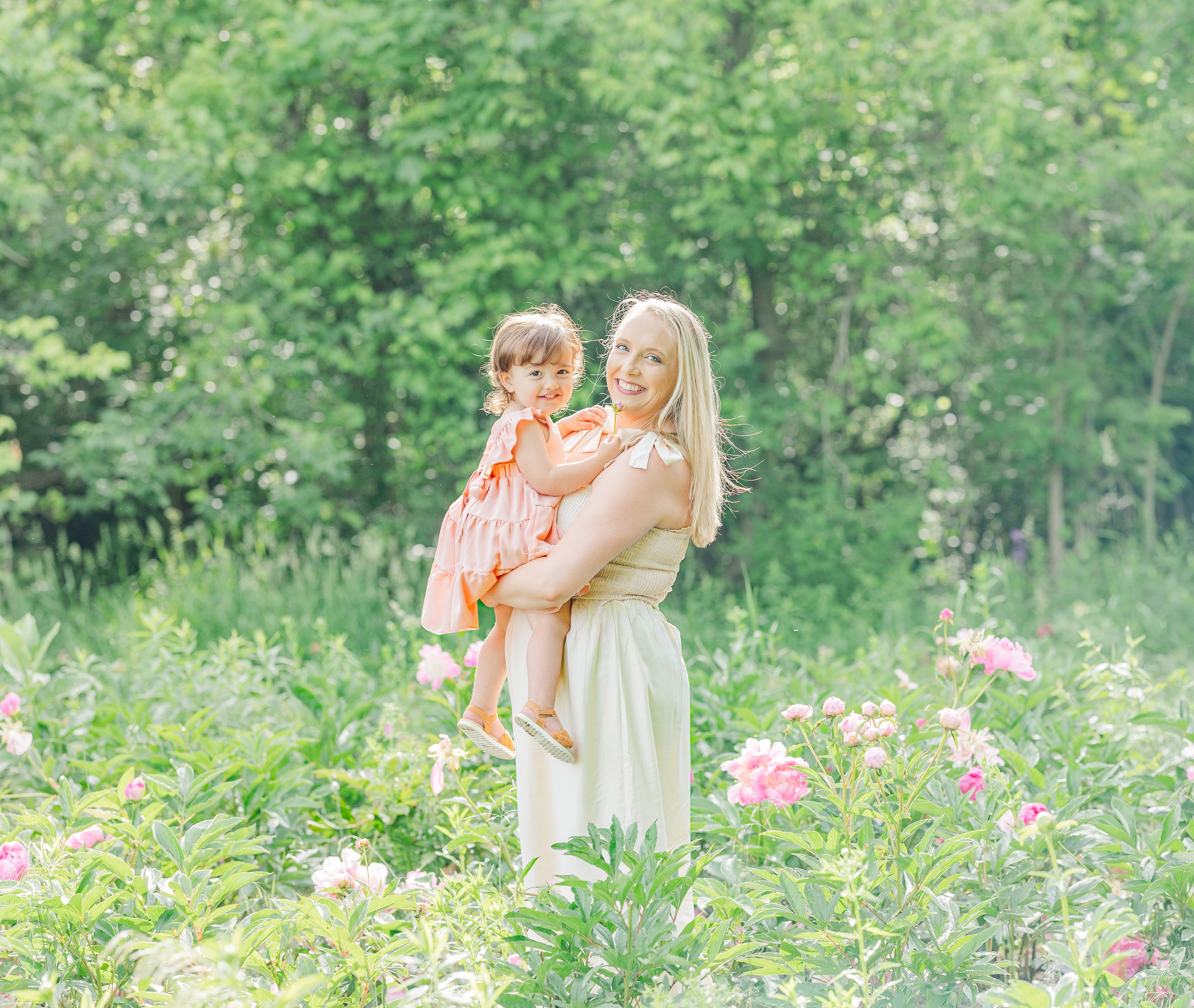 A happy mom stands among pink flowers holding her toddler daughter before finding ann arbor kid friendly restaurants