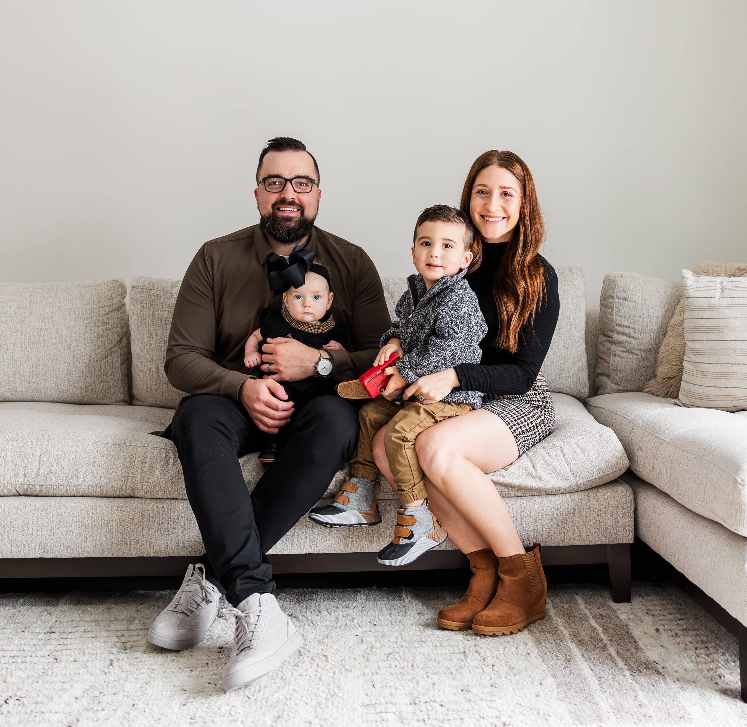 Smiling mom and dad sit on a couch with their baby daughter and toddler son in their laps after some baby classes in ann arbor