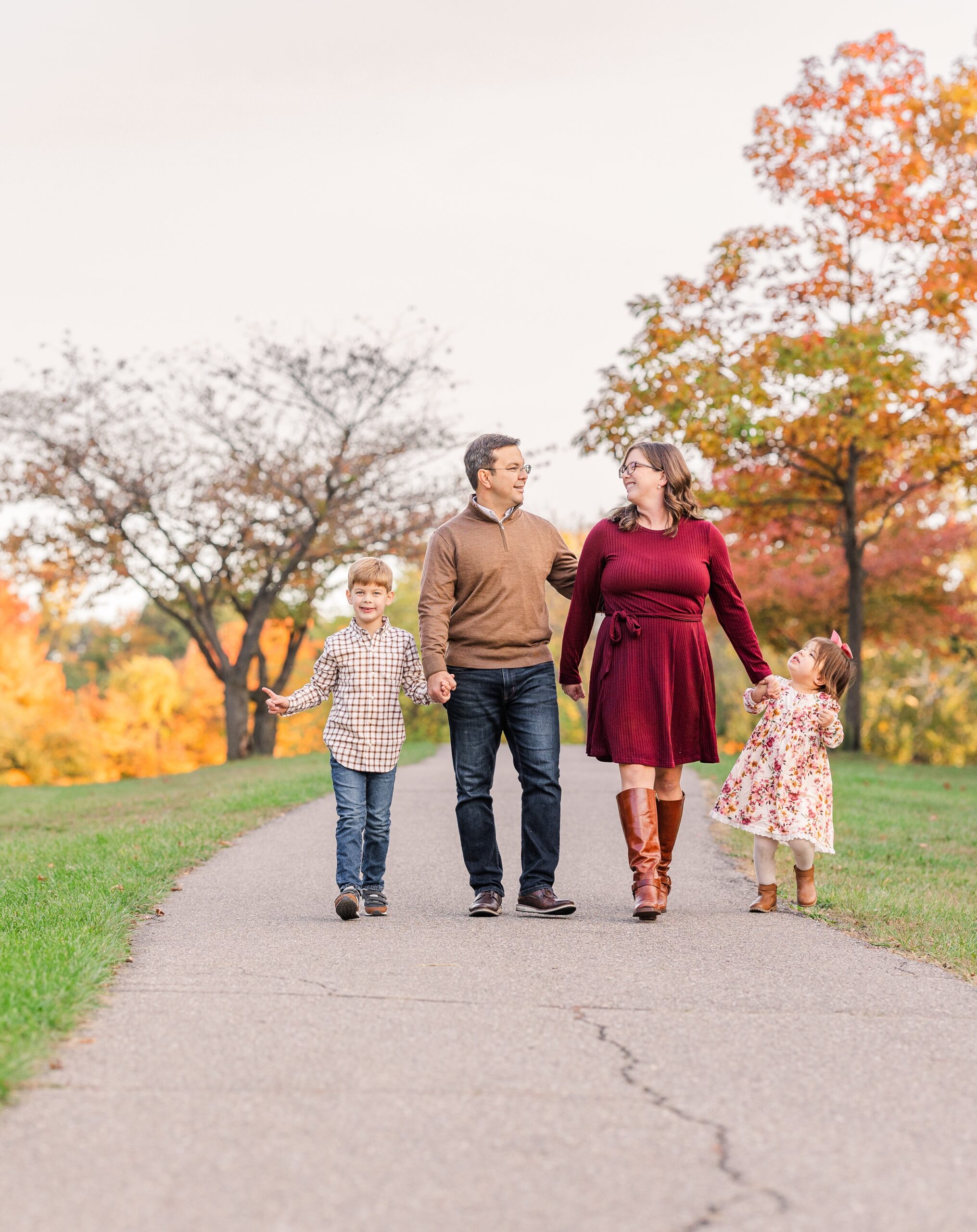 Happy mom and dad hold hands while walking in a park in fall with their toddler son and daughter after some parenting classes in ann arbor