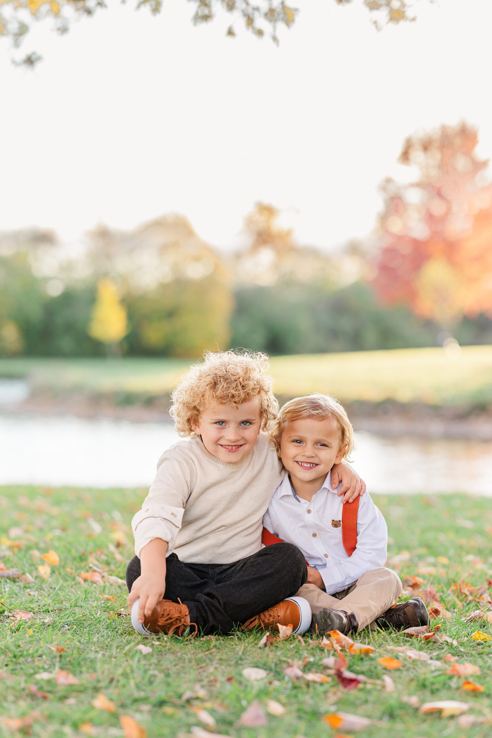 Happy young brothers sit in a park by a pond with arms around each other