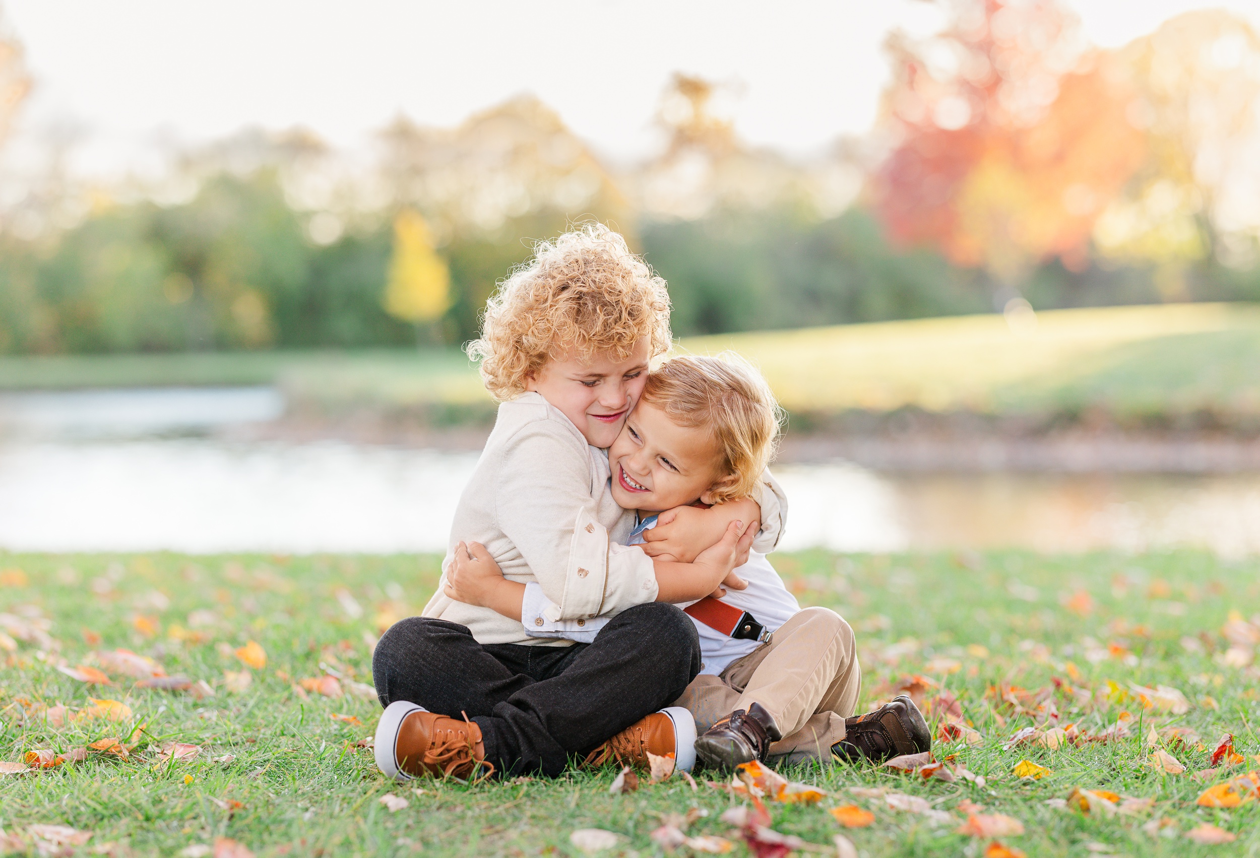 Two toddler brothers sit cross legged in a park lawn at sunset hugging tightly after some toddler classes in ann arbor